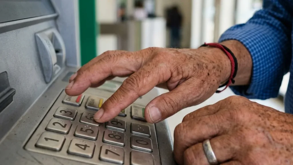Manos de adulto mayor digitando código en el teclado metálico de un cajero bienestar